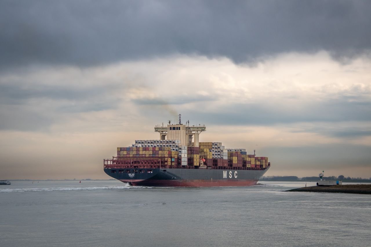 Cargo ship loaded with containers sailing on a calm sea under overcast skies.