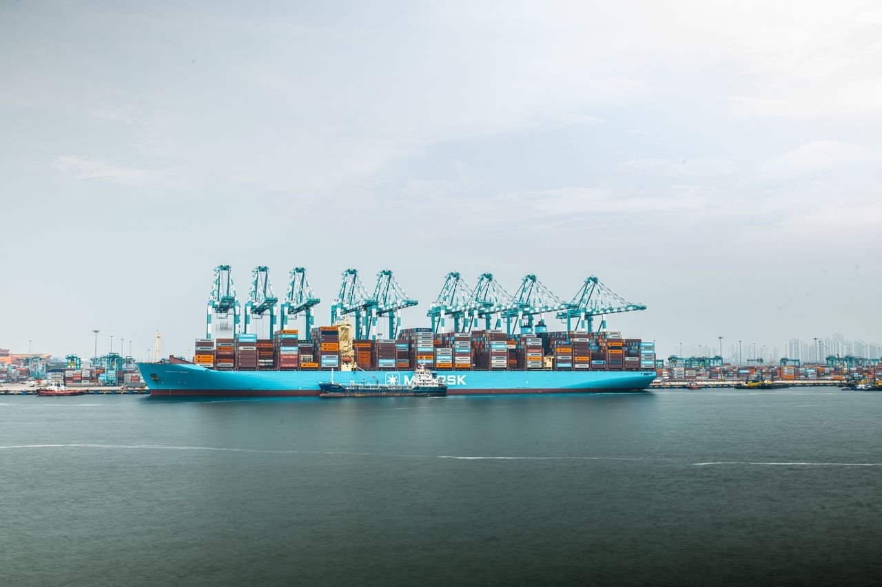 A massive shipping vessel loaded with containers docked at a busy industrial port.